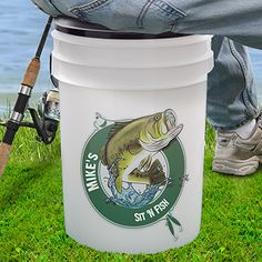 a man holding a fishing rod and a bucket with a fish on it sitting in the grass