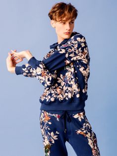 a young man is posing for the camera wearing blue floral pants and a hoodie