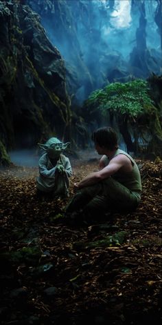 a man sitting on the ground next to a baby yoda in front of some trees