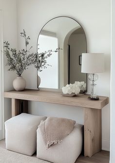 a wooden table topped with a mirror and vase filled with flowers next to a white couch