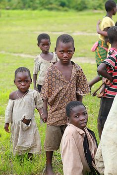 a group of young children standing next to each other on a lush green grass covered field