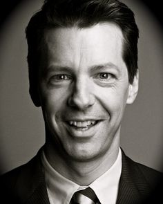 a black and white photo of a man in a suit smiling at the camera with a smile on his face