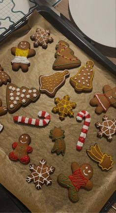 a pan filled with lots of different decorated cookies on top of a wooden table next to plates and utensils