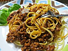 a white plate topped with pasta and meat covered in sauce next to spinach leaves