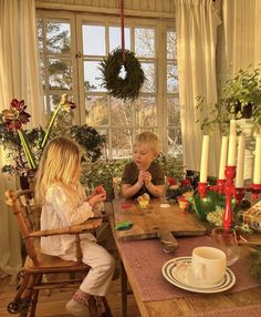 two young children sitting at a table in front of a window with christmas decorations on it