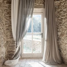 an open window in a stone building with curtains hanging from it's windowsill