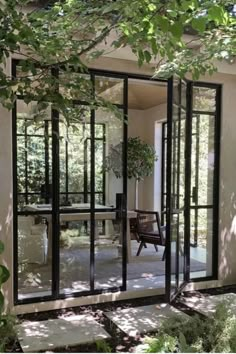 an open glass door leading into a patio area with chairs and trees in the background