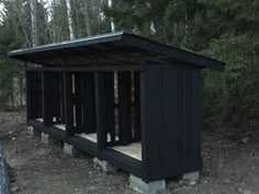 a small black outhouse sitting in the middle of a forest