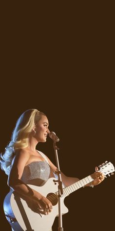 a woman holding a guitar and singing into a microphone