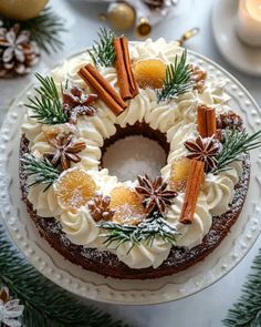 a cake decorated with oranges and cinnamon on a white plate next to christmas decorations