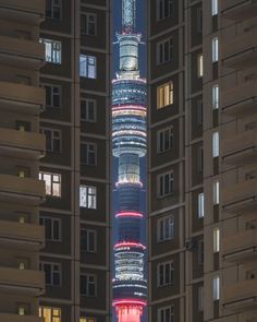 a tall building lit up at night in the middle of a city with other buildings around it