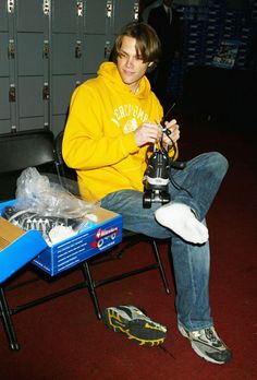 a young man sitting on a chair with a machine in his hand and some shoes next to him