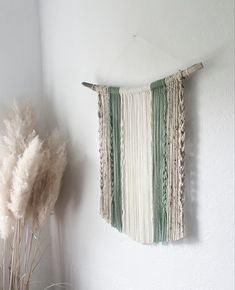 a wall hanging made out of yarn next to a vase with dried grass in it