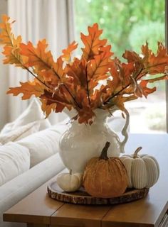 a white vase filled with orange and yellow leaves sitting on top of a wooden table