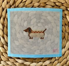 a cross - stitch dachshund on a blue and white cloth in a woven basket