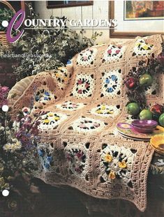 an old fashioned crocheted blanket with flowers and fruit on the table next to it