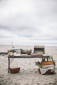 a picnic table set up on the beach with food and drinks laid out in baskets