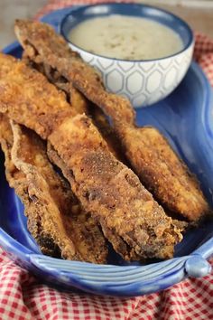 fried fish sticks on a blue plate next to a bowl of ranch dressing and a red checkered tablecloth