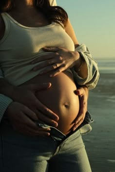 a pregnant woman is holding her belly in front of the ocean