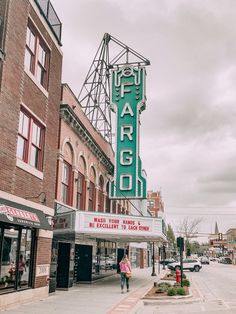 a woman walking down the street in front of a theater marquee on a cloudy day