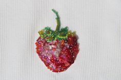 a strawberry shaped brooch sitting on top of a white cloth