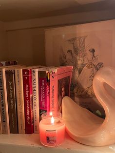 a candle and some books are sitting on a shelf in front of a swan statue