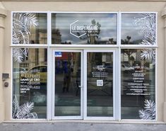 the front door of a building with palm leaves on it's glass doors and windows