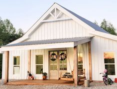 a small white house with two bikes parked on the front porch and one door open