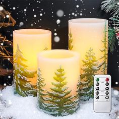 three lit candles sitting on top of snow covered ground next to a christmas tree and remote control