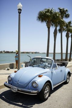 an old blue beetle parked on the side of the road next to some palm trees