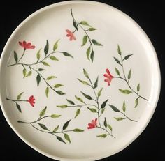 a white plate with red flowers and green leaves painted on the side, against a black background