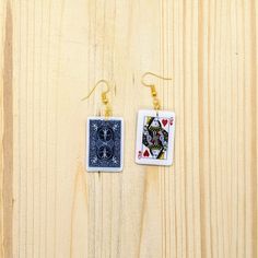 two square earrings with playing cards hanging from them on a wooden surface, one is blue and the other is white