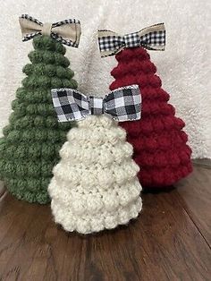 three small crocheted christmas trees with bows on each one, all in different colors