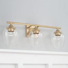 three light bathroom fixture with clear glass globes and brass finish on the top shelf