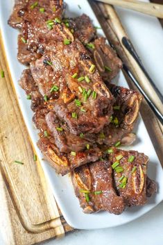 some meat on a white plate with chopsticks next to it and another dish in the background