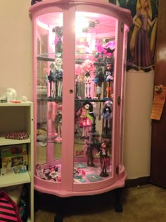 a pink display case filled with lots of dolls and toys in a room next to a book shelf