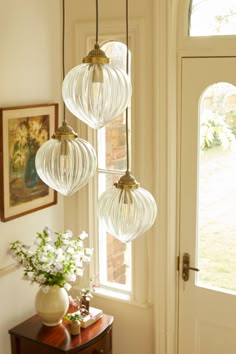 three glass globes hanging from the ceiling above a table with flowers in front of it