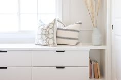 a white shelf with two pillows on top of it and some books in front of the window