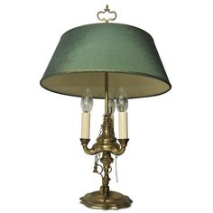 a brass table lamp with a green shade on the top and two white candles underneath