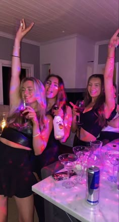 three girls are posing for the camera with their arms in the air while holding up wine glasses