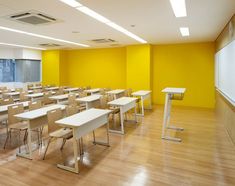 an empty classroom with yellow walls and white desks