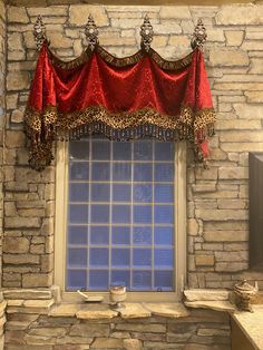 a stone wall with a window and red curtains on the windowsill in front of it