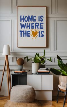 a living room with white walls and wooden flooring, a large poster on the wall that says home is where the is