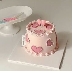 a pink birthday cake with hearts on it and a small toothbrush next to it