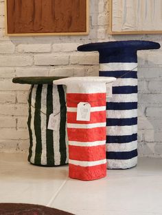 three different colored vases sitting next to each other on a white counter top in front of a brick wall