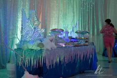 a table topped with lots of cakes and desserts covered in icing next to a curtain