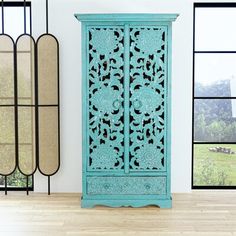 a tall blue cabinet sitting in front of two large windows next to each other on top of a hard wood floor