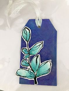 a blue tag with a green plant on it and white ribbon hanging from the side