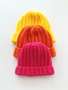 three knitted beanies sitting next to each other on a white surface in different colors