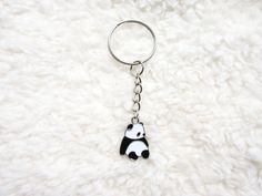 a black and white panda bear keychain sitting on top of a fluffy white blanket